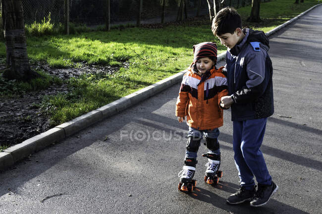 UK, Boy (10-11) supporting brother (4-5) with roller skates — Stock Photo