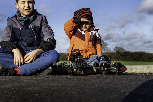 Великобритания, два мальчика (4-5, 10-11) сидят на бордюре — стоковое фото