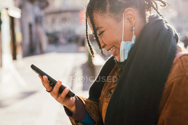 Italia, Mujer sonriente con máscara facial mirando el teléfono inteligente al aire libre - foto de stock