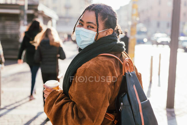Italia, Mujer con máscara facial mirando a la cámara en la calle de la ciudad - foto de stock