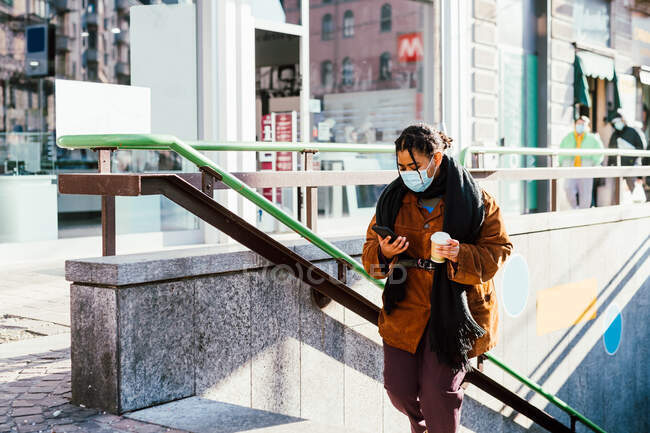 Italien: Frau mit Mundschutz hält Smartphone und Einwegbecher auf Stufen — Stockfoto