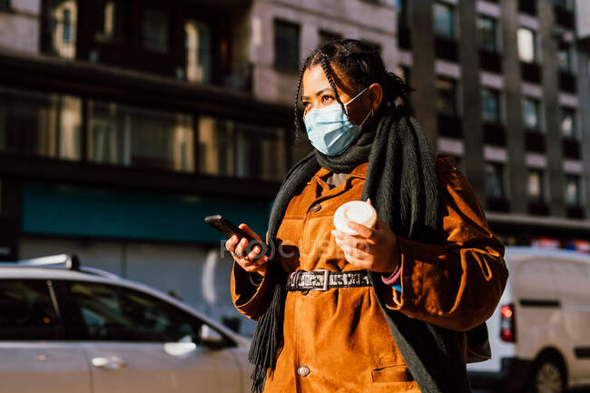 Italia, Maschera donna in faccia con smart phone e tazzina usa e getta in strada — Foto stock