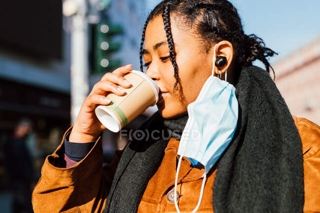 Italia, Mujer joven con mascarilla bebiendo de la taza desechable al aire libre - foto de stock