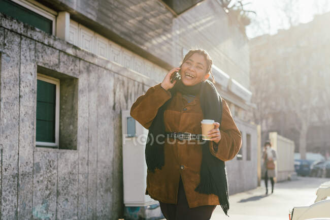 Italie, Femme souriante parlant au téléphone et tenant une tasse jetable dans la rue de la ville — Photo de stock