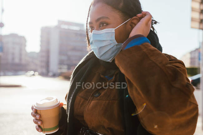 Italia, Mujer joven con mascarilla que sostiene la taza desechable al aire libre - foto de stock