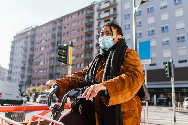 Italy, Young woman in face mask riding bicycle in city — Stock Photo