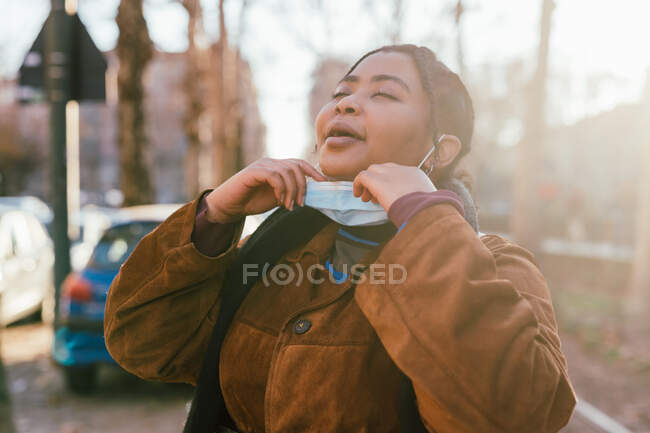 Italia, Mujer joven quitándose la mascarilla al aire libre - foto de stock