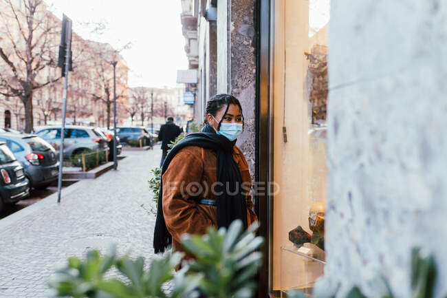 Italy, Young woman in face mask looking at store window — Stock Photo