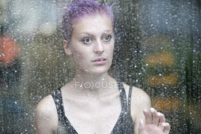 Jeune femme derrière fenêtre mouillée — Photo de stock