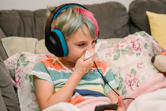 Canada, Ontario, Garçon avec des cheveux colorés et écouteurs soufflant du nez sur le canapé — Photo de stock