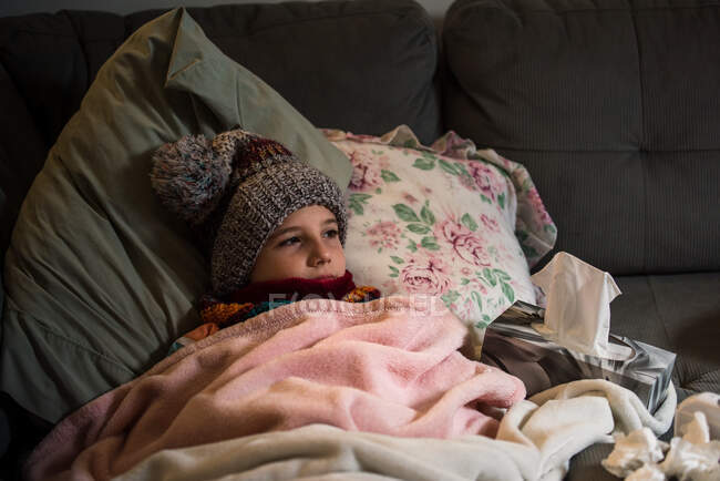 Canada, Ontario, Boy in knit hat lying on sofa covered with blanket — Stock Photo