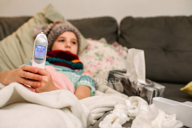 Canada, Ontario, Boy in knit hat holding electronic thermometer on sofa — Stock Photo