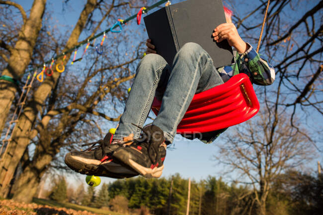 Canadá, Ontário, Visão de baixo ângulo do menino com livro sobre swing — Fotografia de Stock