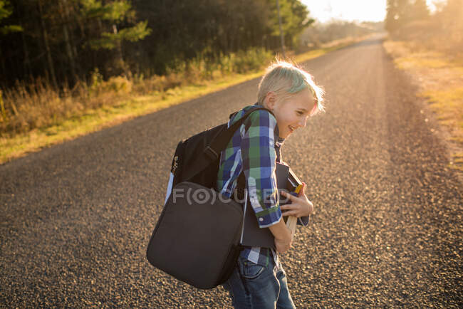 Канада, Онтарио, Смилинг мальчик с книгами о сельской дороге на закате — стоковое фото