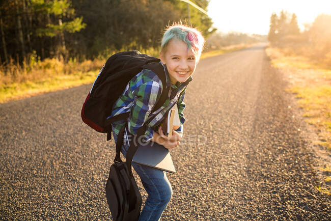 Канада, Онтаріо, усміхнений хлопчик з книжками про сільську дорогу після заходу сонця. — стокове фото