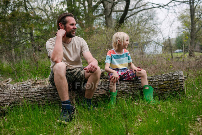 Канада, Онтарио, Кингстон, отец и сын сидят на бревне в лесу — стоковое фото