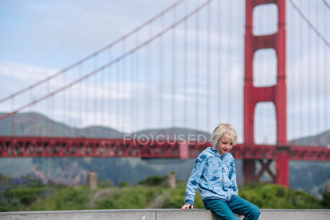 США, Каліфорнія, Сан - Франциско, хлопчик сидить на стіні біля мосту Золоті Ворота. — стокове фото