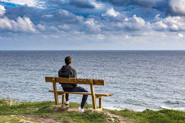 Francia, Bretagne, Finistere sud, Vista trasera del hombre en el banco frente al mar - foto de stock