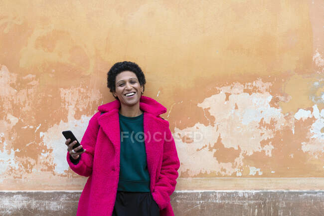 Italia, Toscana, Pistoia, Mujer sonriente de abrigo rosa con teléfono inteligente - foto de stock