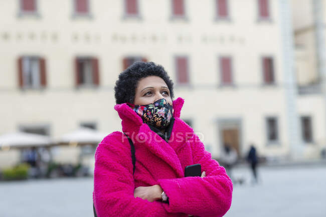 Italy, Tuscany, Pistoia, Woman in face mask and pink coat walking through city — Stock Photo