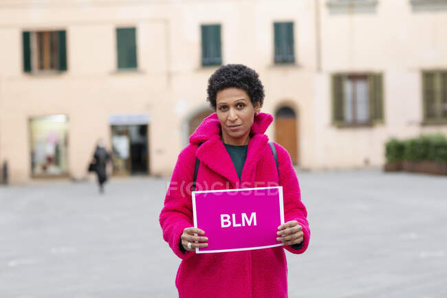 Italia, Toscana, Pistoia, Mujer de abrigo rosa sosteniendo el signo - foto de stock