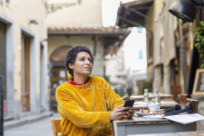 Italia, Toscana, Pistoia, Mujer sentada en la cafetería al aire libre y utilizando el teléfono inteligente - foto de stock