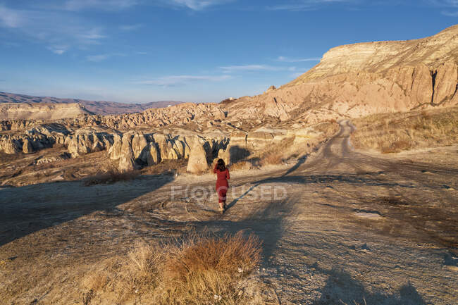 Turquia, Capadócia, Visão traseira da mulher em vestido vermelho andando na paisagem rochosa — Fotografia de Stock