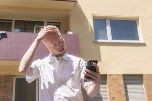 Allemagne, Cologne, Albinos homme en chemise blanche tenant téléphone intelligent — Photo de stock