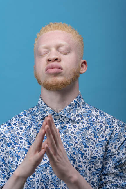 Studio portrait of albino man in blue patterned shirt with eyes closed — Stock Photo