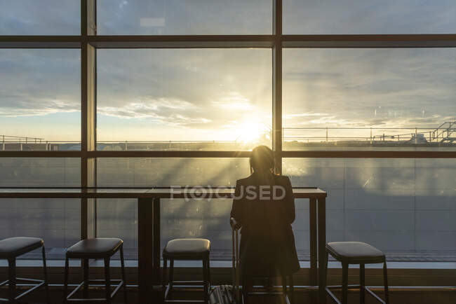UK, London, Rear view of woman at airport terminal at sunset — Stock Photo