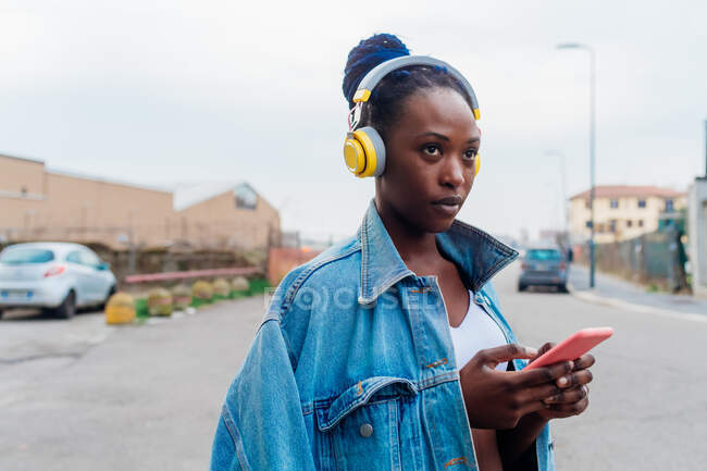 Italien, Mailand, Frau mit Kopfhörer hält Smartphone in der Stadt — Stockfoto