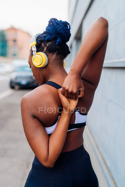 Italy, Milan, Rear view of woman in sports clothing and headphones stretching — Stock Photo
