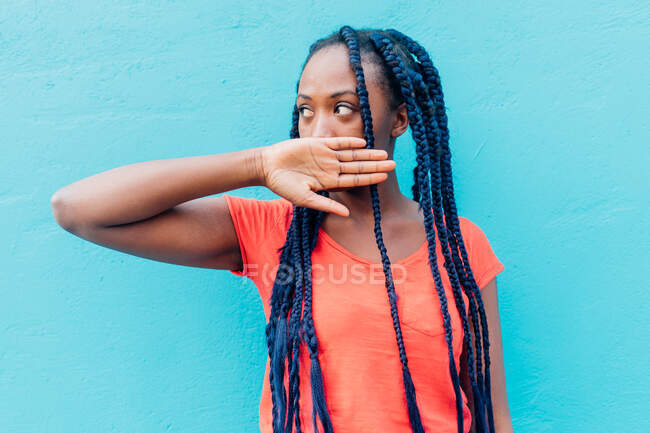 Italy, Milan, Young woman covering mouth in front of blue wall — Stock Photo