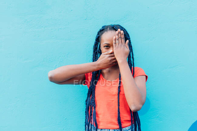 Italy, Milan, Young woman covering mouth and eye in front of blue wall — Stock Photo
