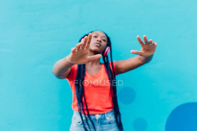Italy, Milan, Young woman with headphones dancing in front of blue wall — Stock Photo