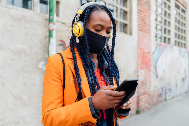 Italien, Mailand, Frau mit Kopfhörer und Mundschutz mit Smartphone — Stockfoto