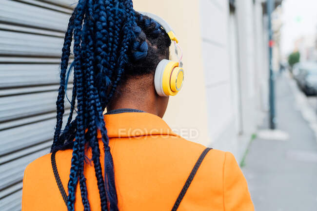 Itália, Milão, Vista traseira da mulher com tranças e fones de ouvido na cidade — Fotografia de Stock