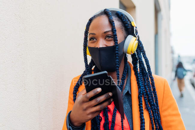 Italia, Milán, Mujer de moda con máscara facial, auriculares y teléfono inteligente - foto de stock