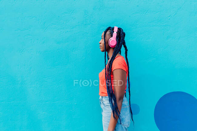 Italy, Milan, Profile of young woman with headphones in front of blue wall — Stock Photo