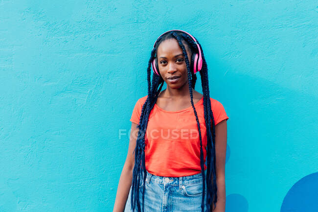 Italy, Milan, Portrait of young woman with headphones in front of blue wall — Stock Photo