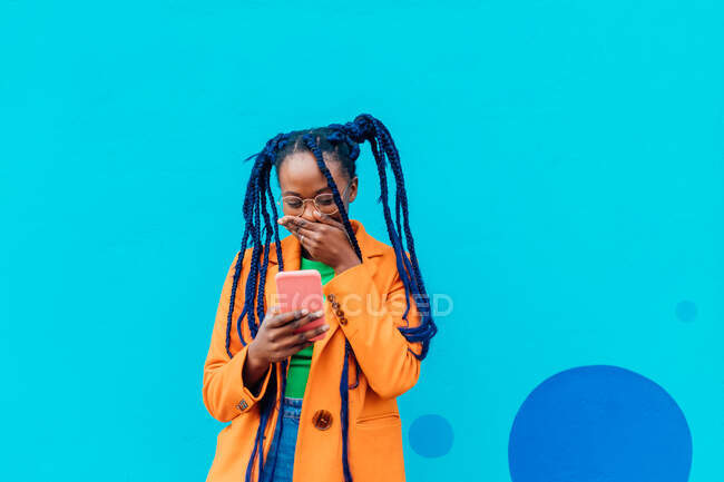 Italy, Milan, Woman with braids using smart phone against blue wall — Stock Photo