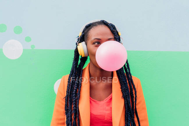 Italy, Milan, Stylish woman with headphones blowing chewing gum against wall — Stock Photo