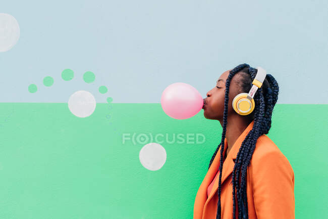 Italy, Milan, Stylish woman with headphones blowing gum against wall — Stock Photo