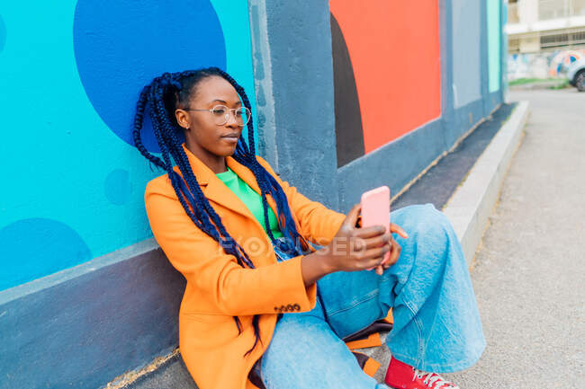 Італія, Мілан, Жінка з плечима сидять біля барвистої стіни, за допомогою смартфона. — стокове фото