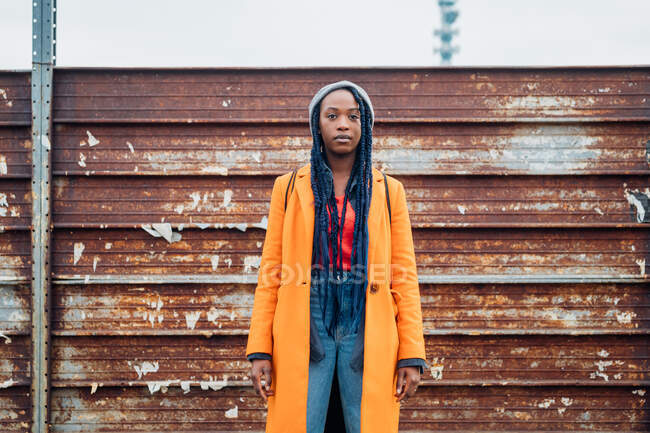 Italia, Milán, Retrato de mujer en abrigo naranja contra valla metálica oxidada - foto de stock