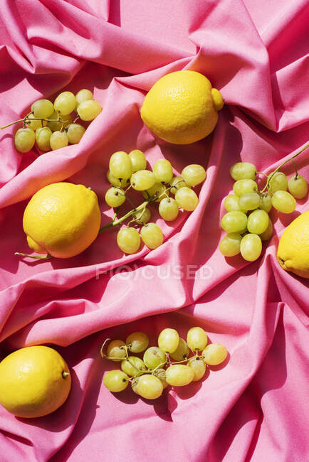 Overhead view of lemons and grapes on pink table cloth — Stock Photo