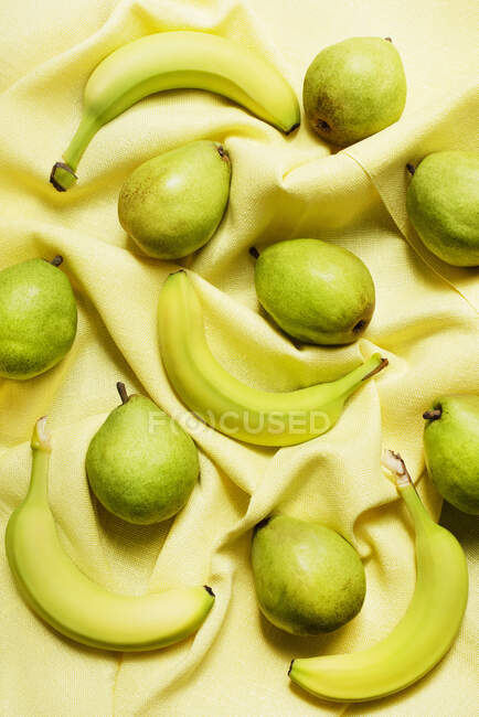 Overhead view of bananas and pears on yellow table cloth — Stock Photo