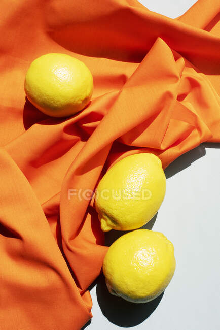 Студійний знімок лимонів і зморщена помаранчева настільна тканина — стокове фото