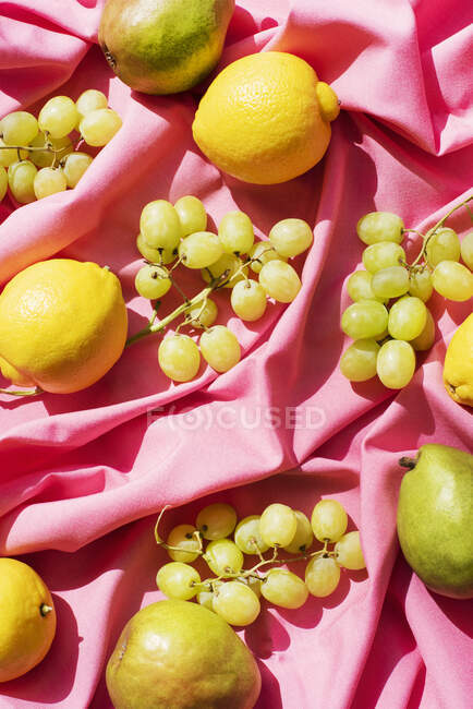 Vista aérea de limones, peras y uvas sobre mantel rosa - foto de stock