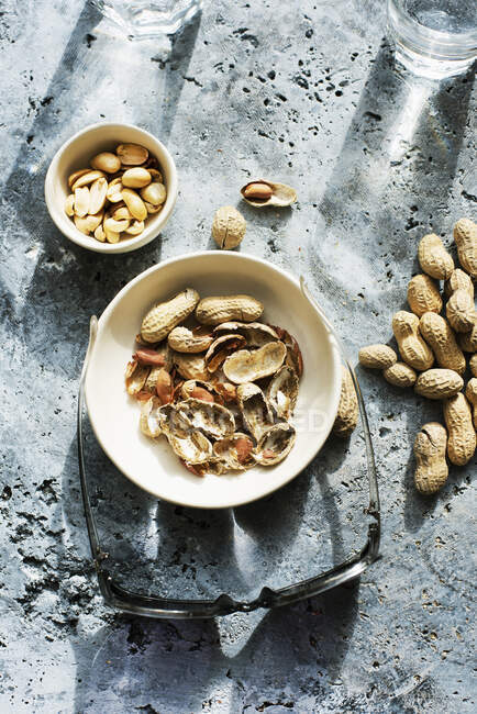 Overhead view of bowls with peanuts and sunglasses on concrete surface — Stock Photo